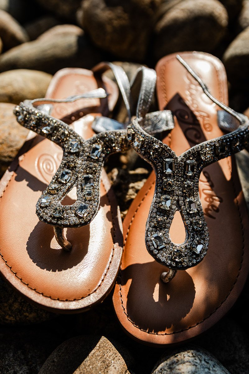 Elegant sandals with rhinestone-encrusted straps glistening in sunlight on a rocky surface, conveying a sense of luxury and summer relaxation.