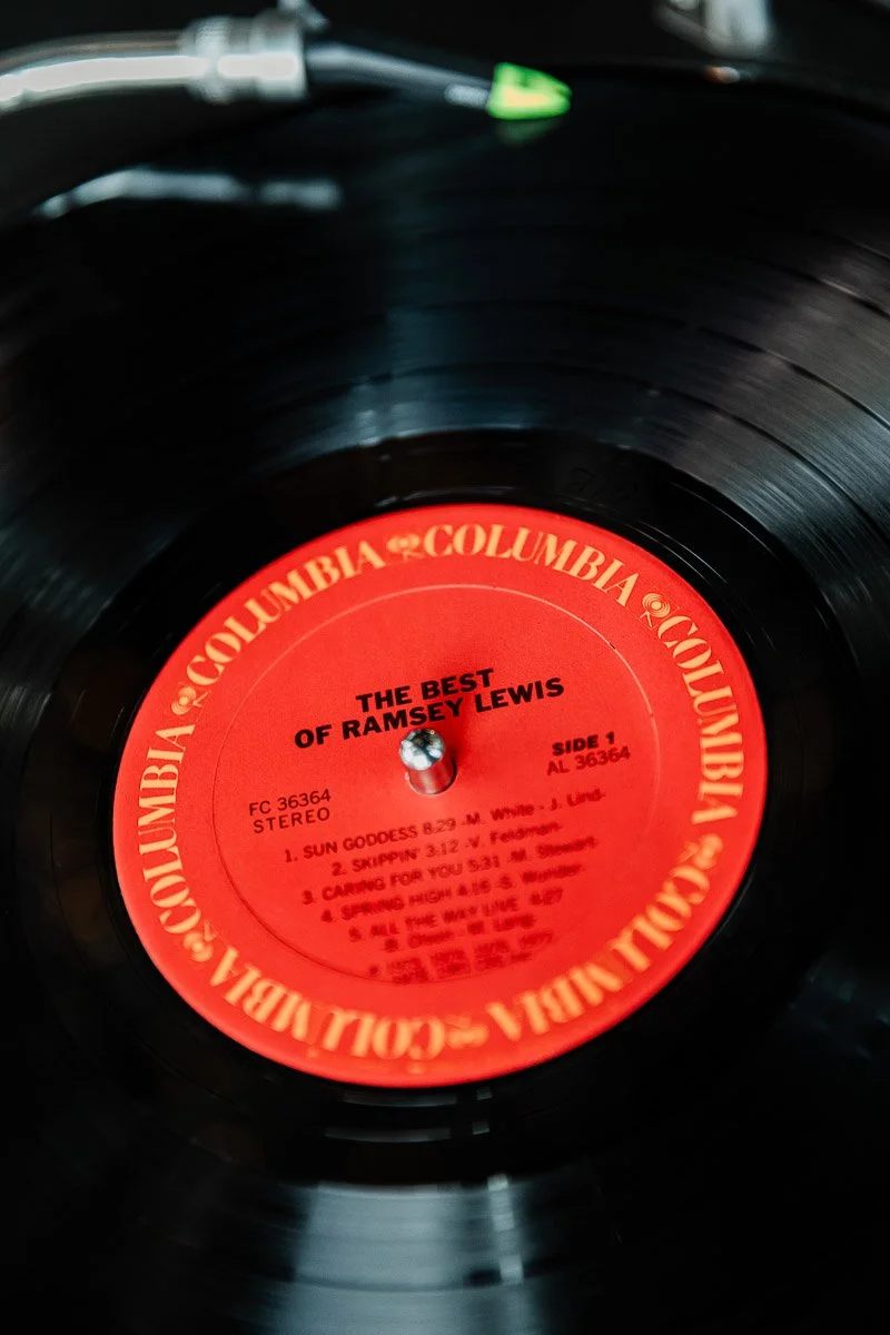 Close-up of a vinyl record spinning on a turntable. The red label reads "The Best of Ramsey Lewis" by Columbia Records, evoking nostalgia.