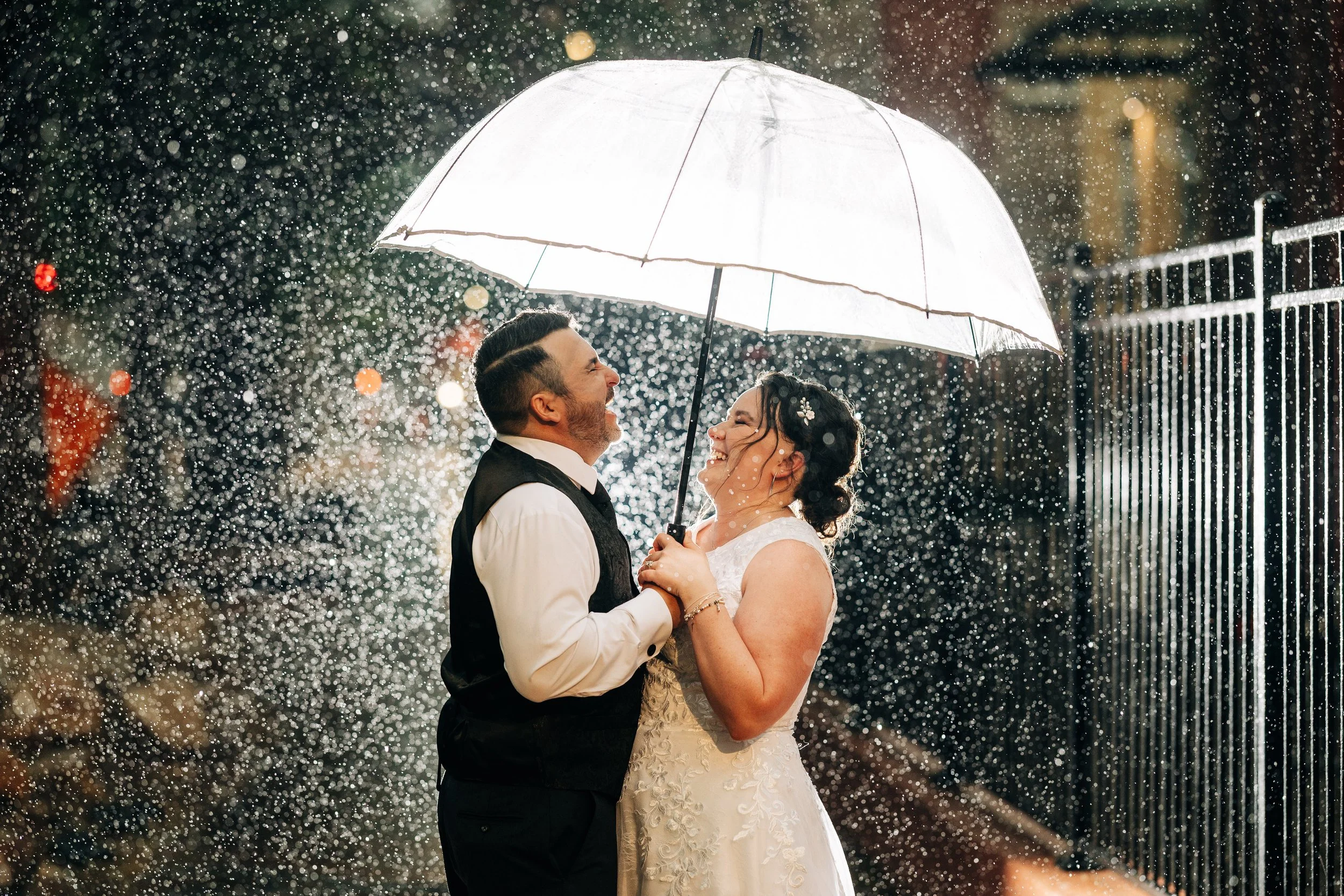Bride and groom laugh under an umbrella in the rain after a Holy Ghost church wedding in Denver, Colorado