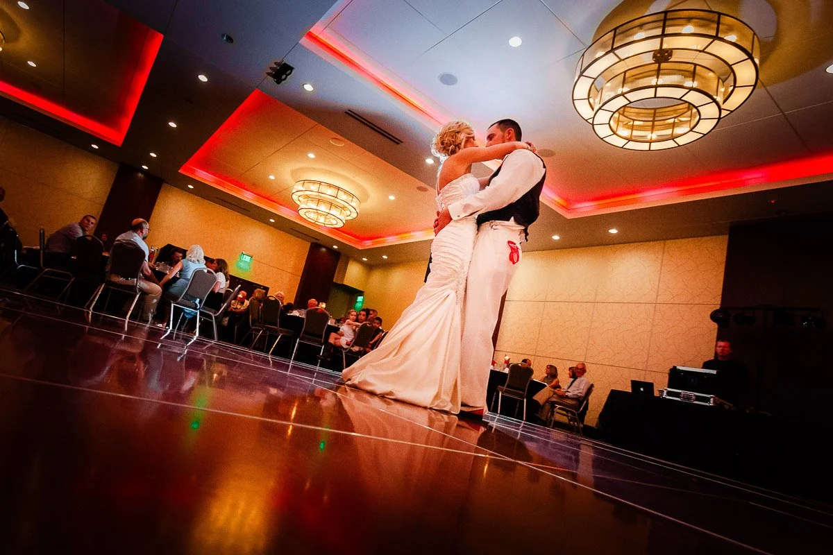 A couple dances closely in a warmly lit ballroom, surrounded by seated guests. Soft red lighting adds a romantic, intimate atmosphere at a Lincoln Center wedding in Fort Collins