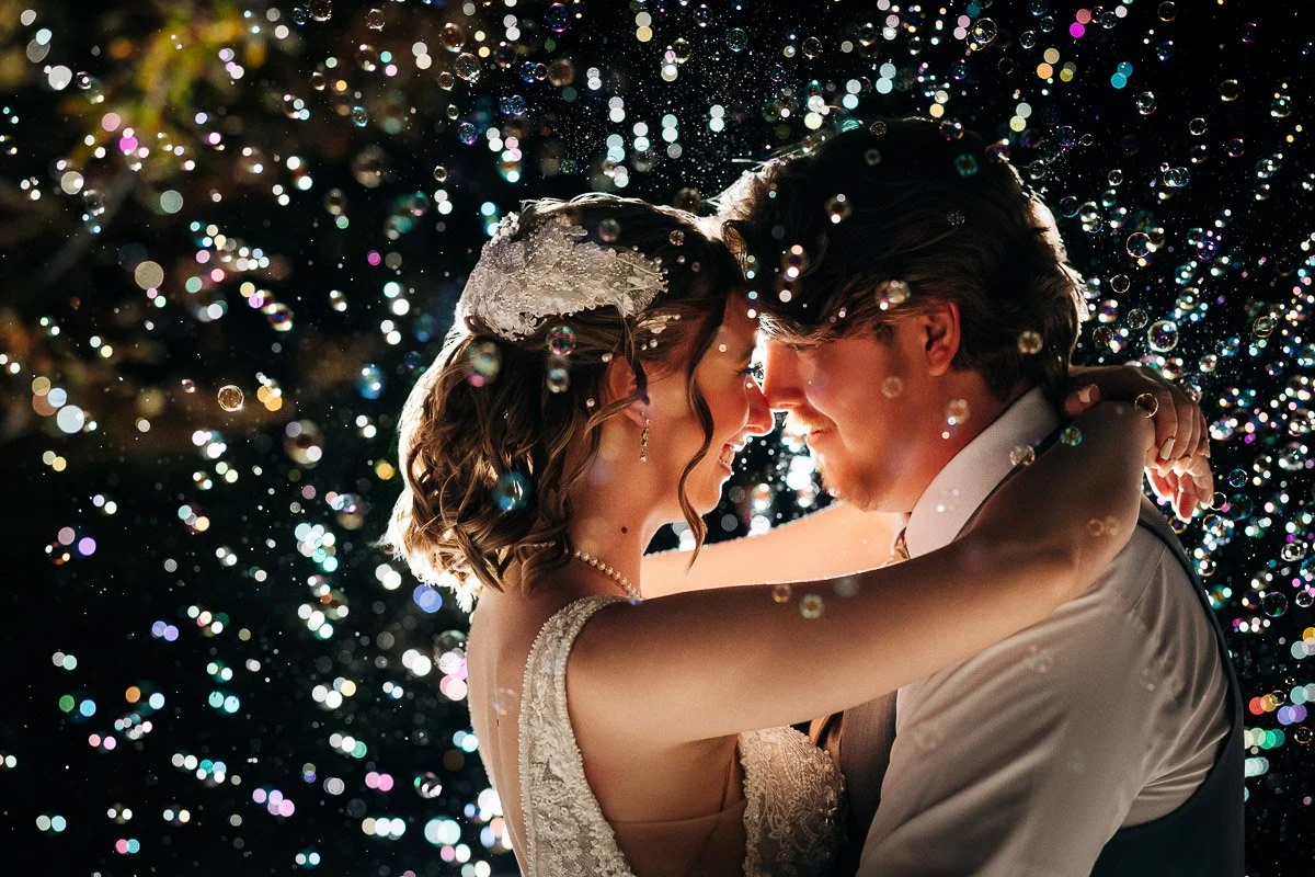 A newlywed couple embraces under a shower of sparkling lights, creating a magical, romantic atmosphere. Smiling faces are illuminated softly during a Greenbriar Inn wedding reception in Boulder, Colorado