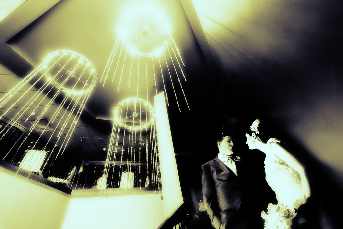 A couple, bathed in ethereal yellow light, gaze at each other in a sophisticated setting with sparkling chandeliers, creating a romantic atmosphere.