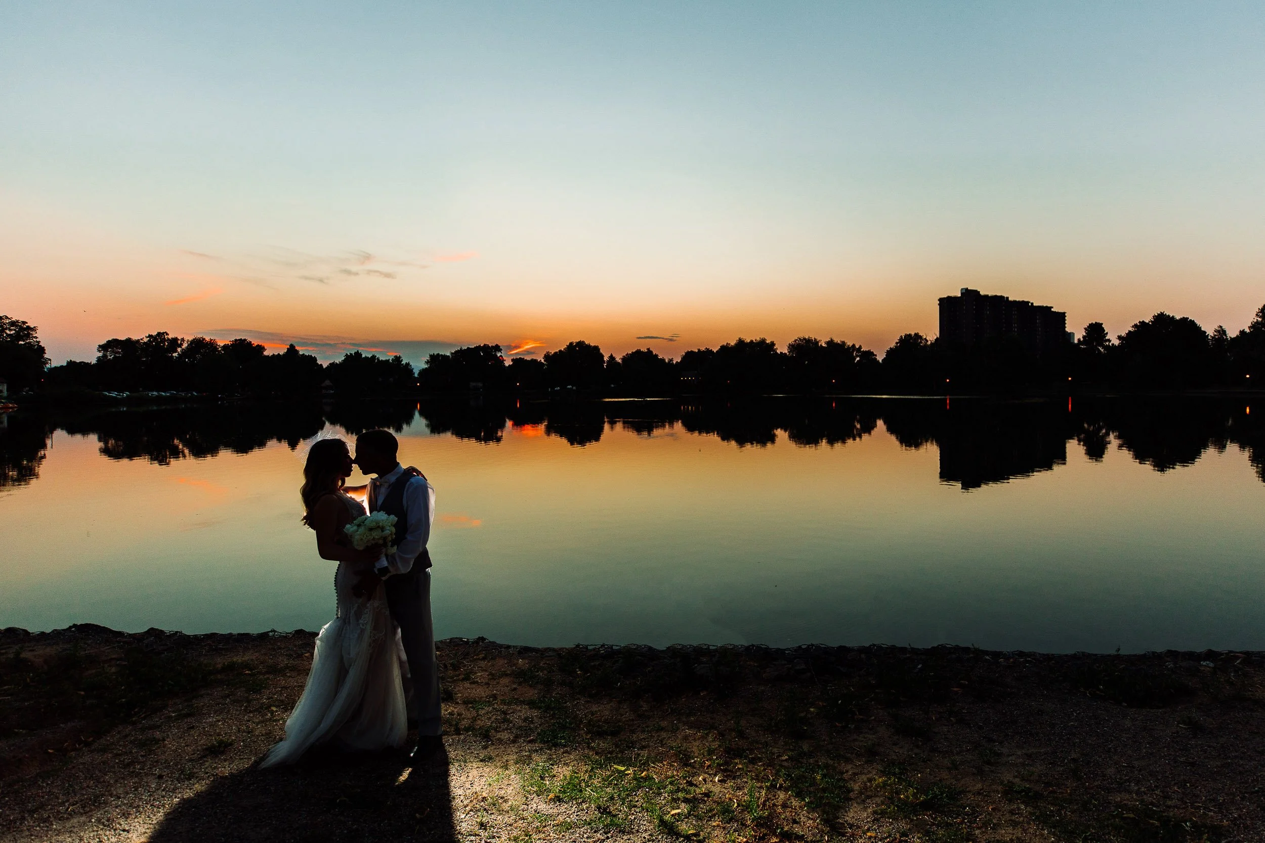 Bride and groom embrace with the water's reflection in the background during a Washington Park Boathouse wedding in Denver, Colorado
