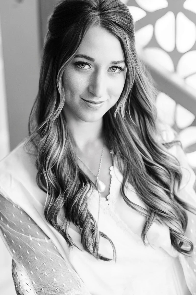 Black and white portrait of a woman with long, wavy hair wearing a light dress. She smiles slightly, exuding a calm and friendly demeanor.