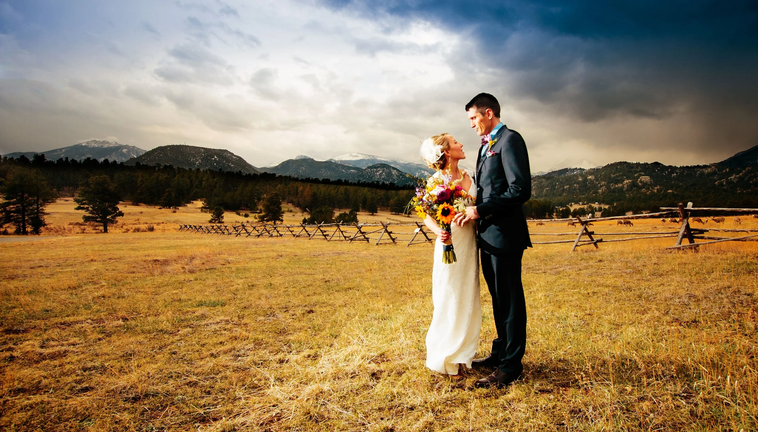 A very tall groom and very short bride embrace with a panoramic mountain range in the background after a Black Canyon Inn wedding in Estes Park, Colorado