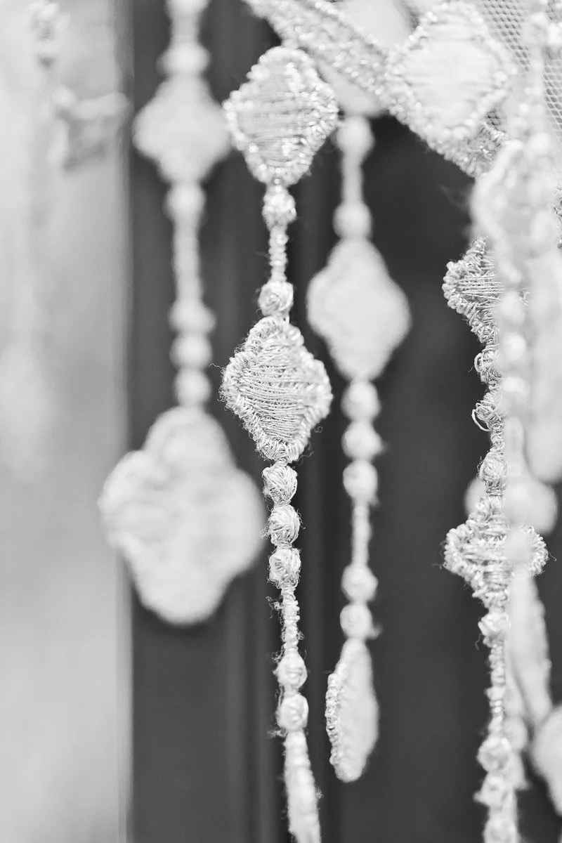 Close-up of intricate, ornate lacework featuring diamond-shaped patterns with delicate textures. The black and white image exudes elegance and timelessness.
