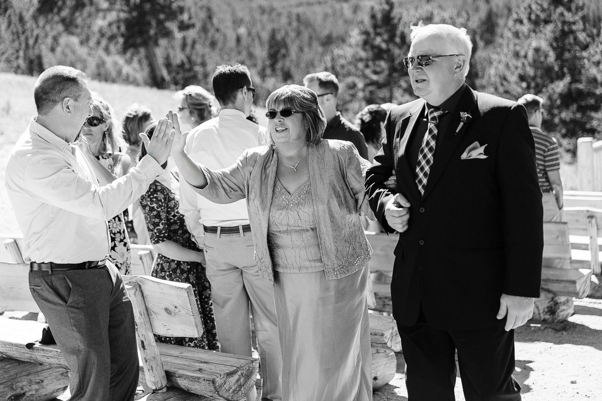 

A group of smiling people outdoors, a woman in sunglasses gives a high-five, surrounded by others in formal attire, trees in the background.