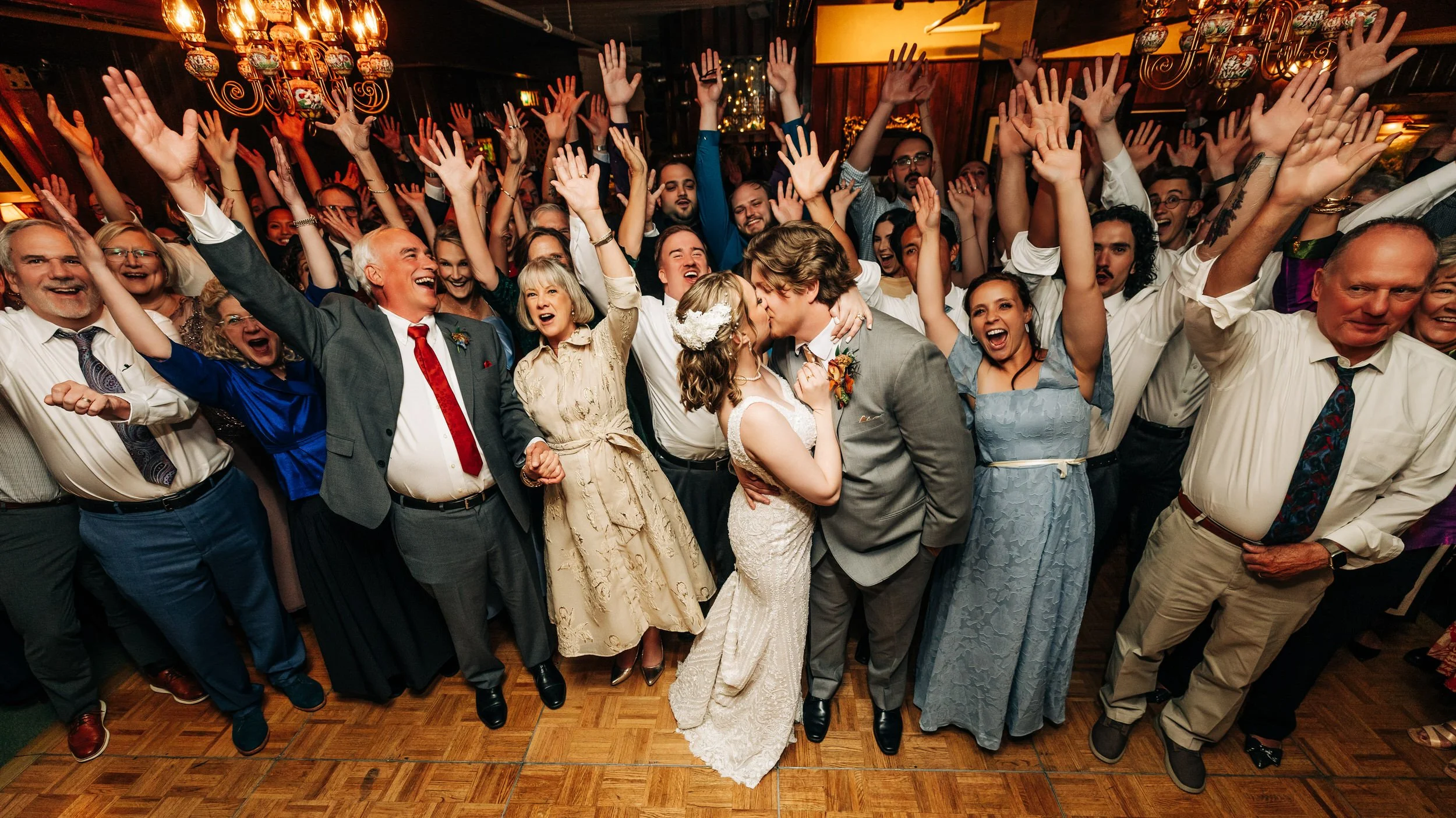 A hundred intoxicated wedding guests cheer on a bride and groom kissing during a Greenbriar Inn wedding reception in Boulder, Colorado