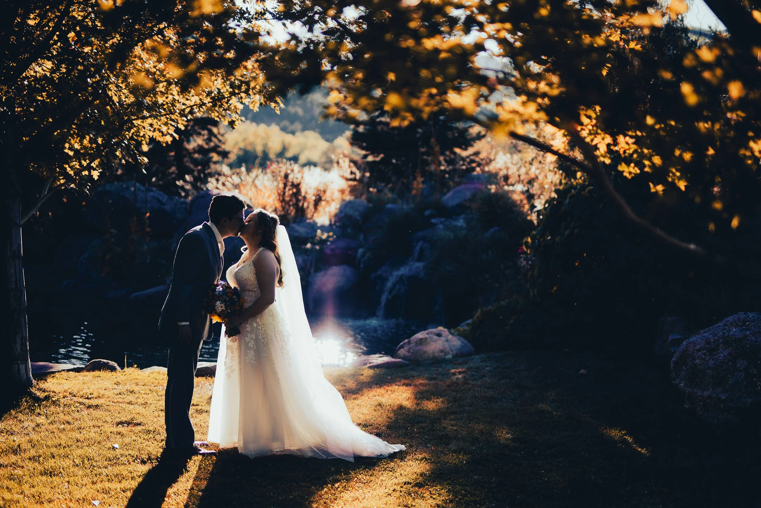 Bride and groom steal a kiss under the trees during a Greenbriar Inn wedding reception in Boulder, Colorado