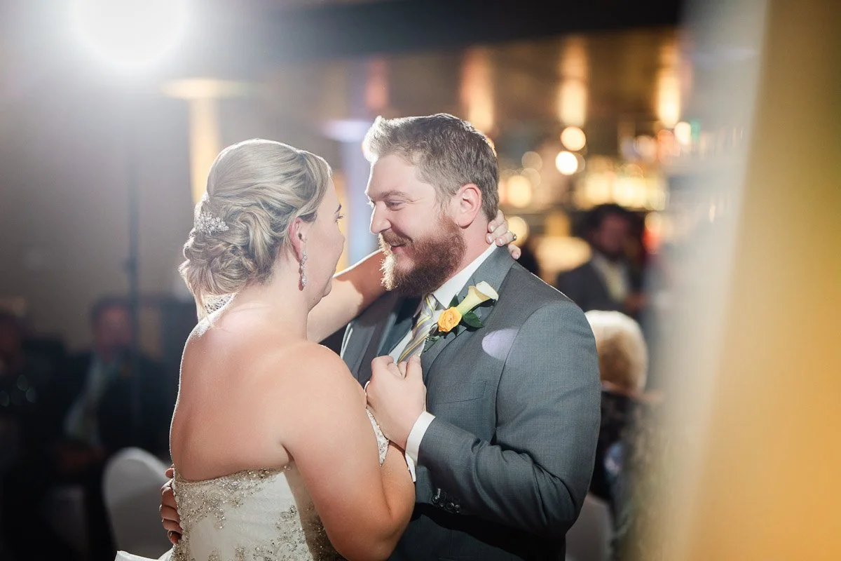 A couple shares a joyful dance at their wedding. The bride in a white dress and the groom in a suit embrace, smiling warmly under soft lighting.