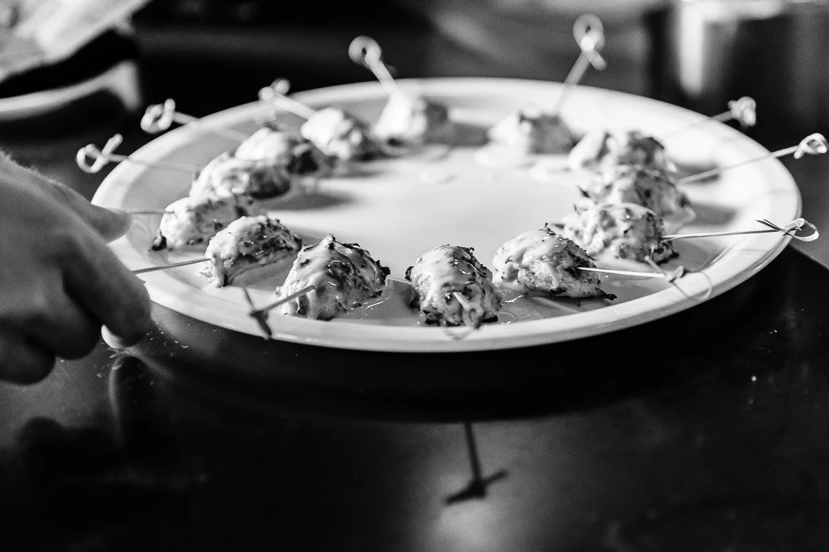 A black and white image of a hand holding a plate with skewered bite-sized appetizers arranged in a circle, creating an elegant and inviting display.