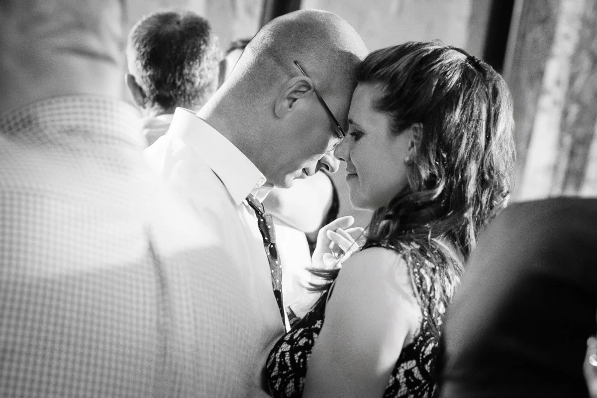 A couple, eyes closed and foreheads touching, share a tender moment while slow dancing. The black-and-white photo conveys warmth and intimacy.