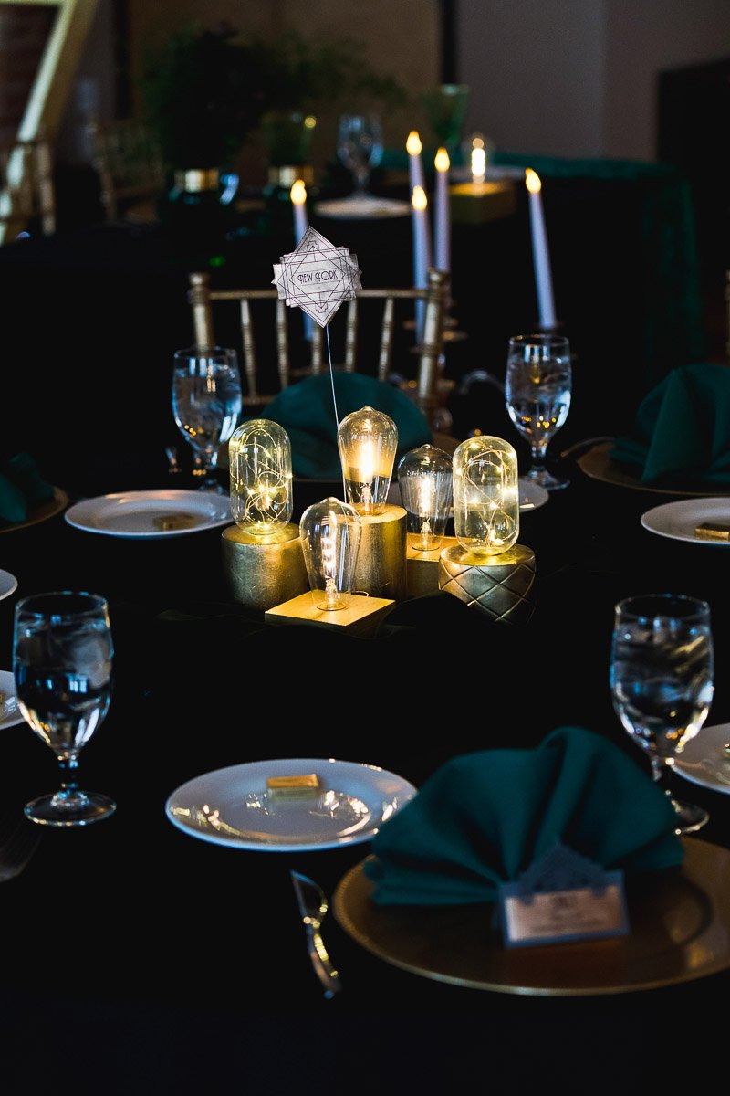 Elegant table setting with glowing vintage bulbs as centerpiece, surrounded by plates, green napkins, and glassware, conveying a warm ambiance.
