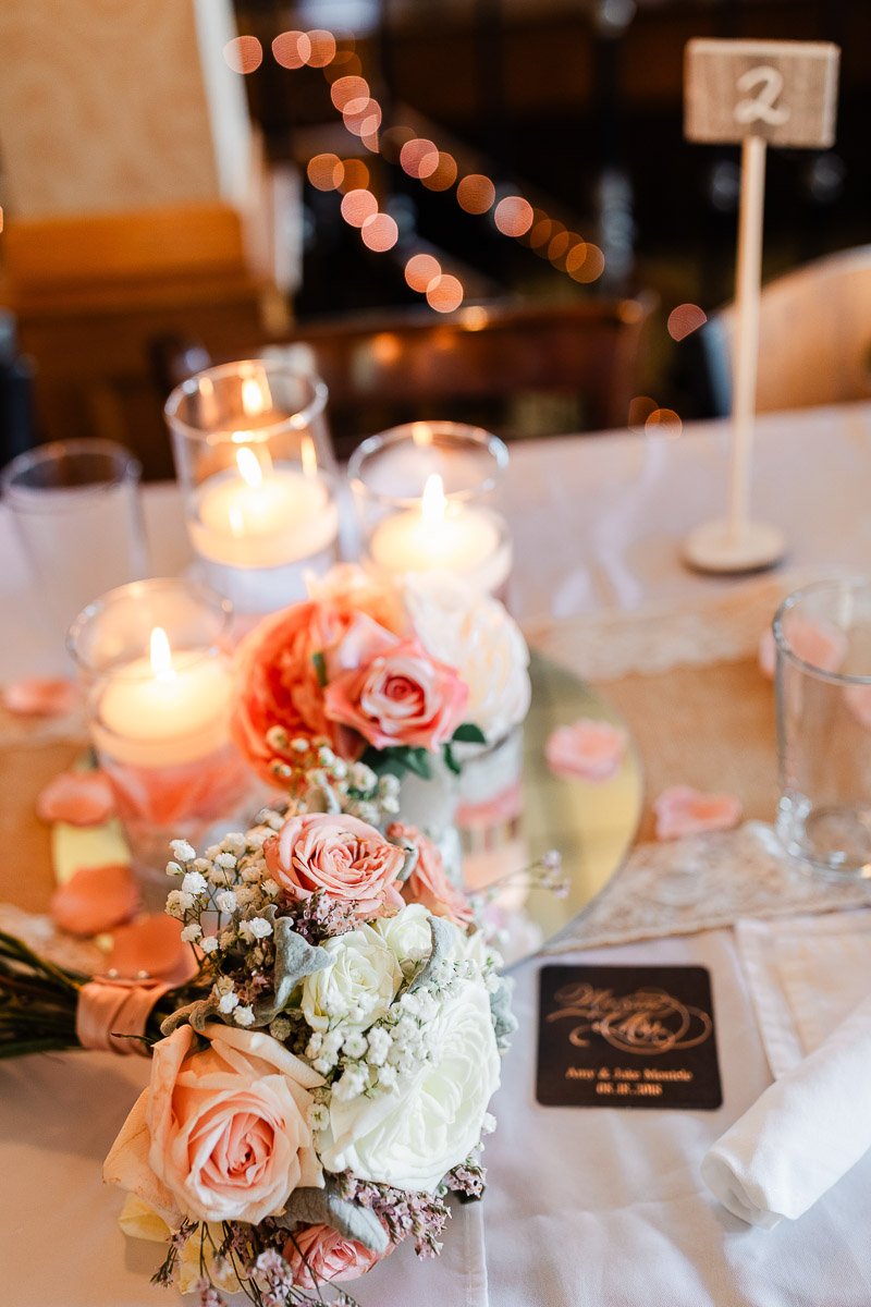 Elegant wedding table setup with lit candles, pink roses, and baby's breath on a mirrored centerpiece. Soft, romantic lighting enhances the ambiance.