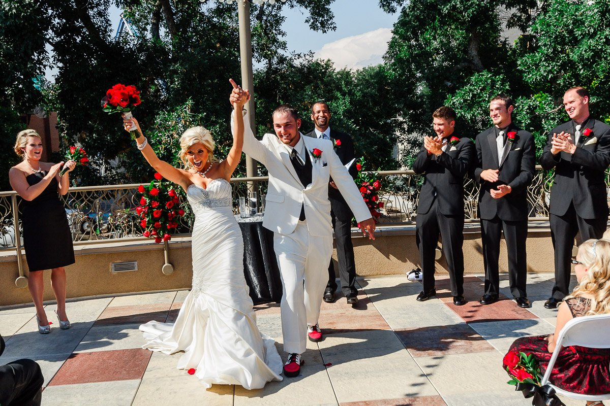 A joyful wedding scene where a bride in a white gown and a groom in a white suit, both holding up a bouquet and hand, celebrating with guests clapping at a Lincoln Center wedding in Fort Collins, Colorado