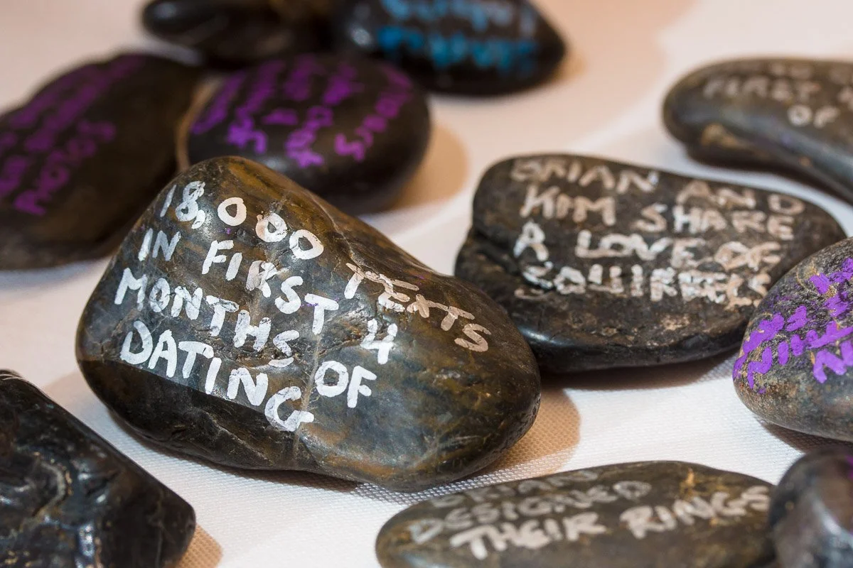 Close-up of smooth black stones with handwritten white and purple messages about love and relationships on a light surface, evoking warmth and sentiment.