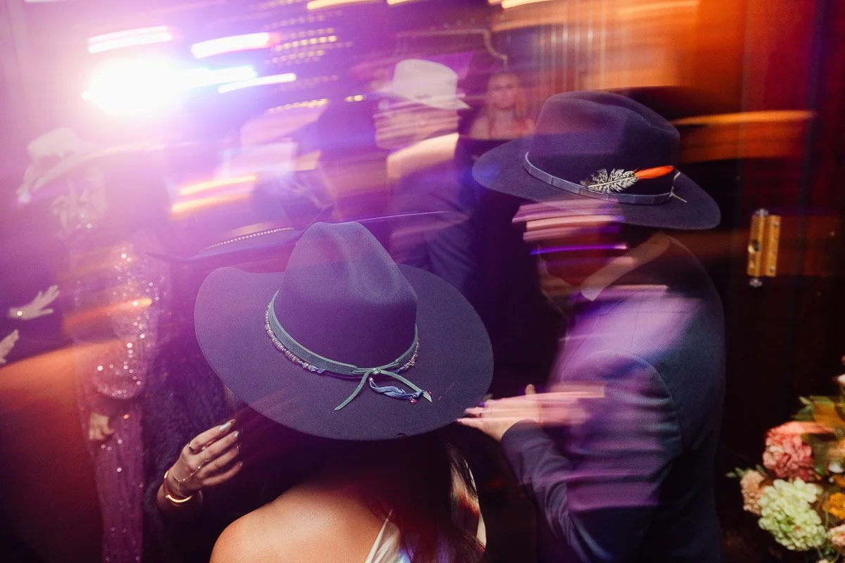 People wearing stylish hats, blurred motion conveying energy, vibrant lights around. Festive and dynamic atmosphere at a party or event.