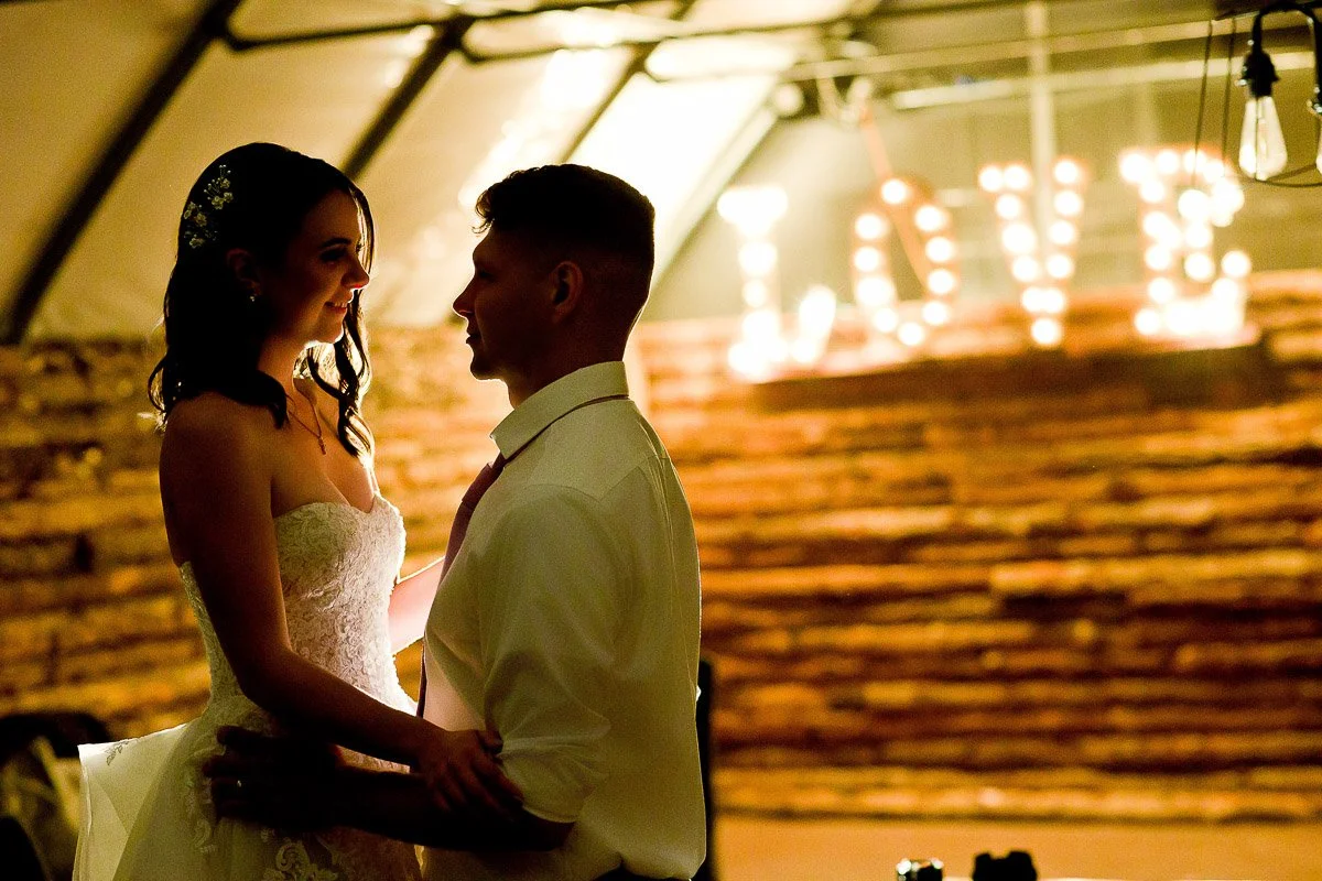 A bride and groom share an intimate dance under soft lighting, with "LOVE" illuminated in the background. The mood is romantic and warm during a Church Ranch Event Center wedding in Westminster, Colorado