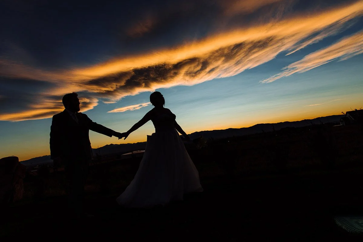 Silhouetted couple holding hands against a dramatic sunset. The sky features vibrant orange clouds, conveying a romantic and serene atmosphere.