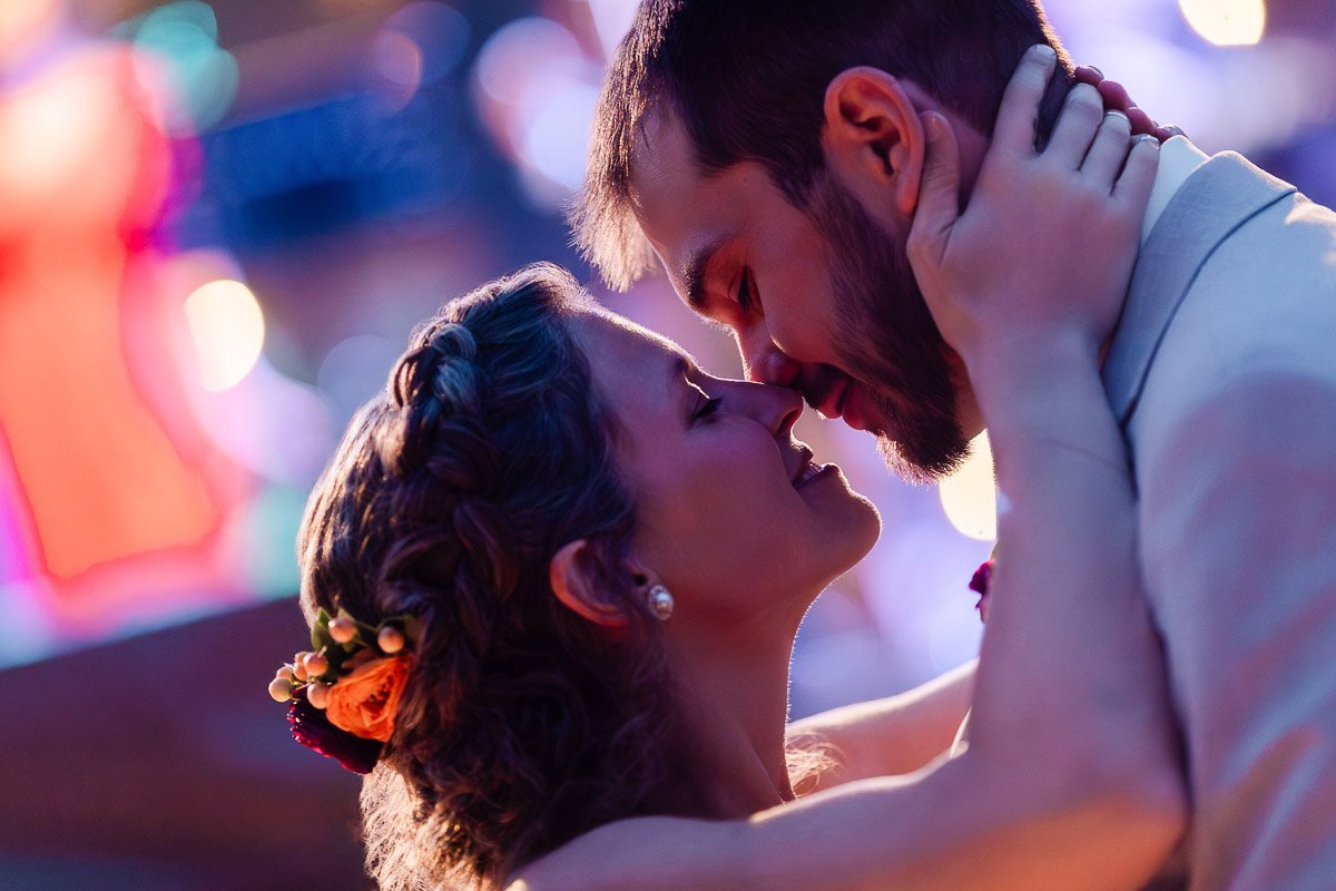 A couple embraces closely, their foreheads touching, bathed in romantic, warm lighting. The woman wears flowers in her braided hair, adding to the intimate mood.