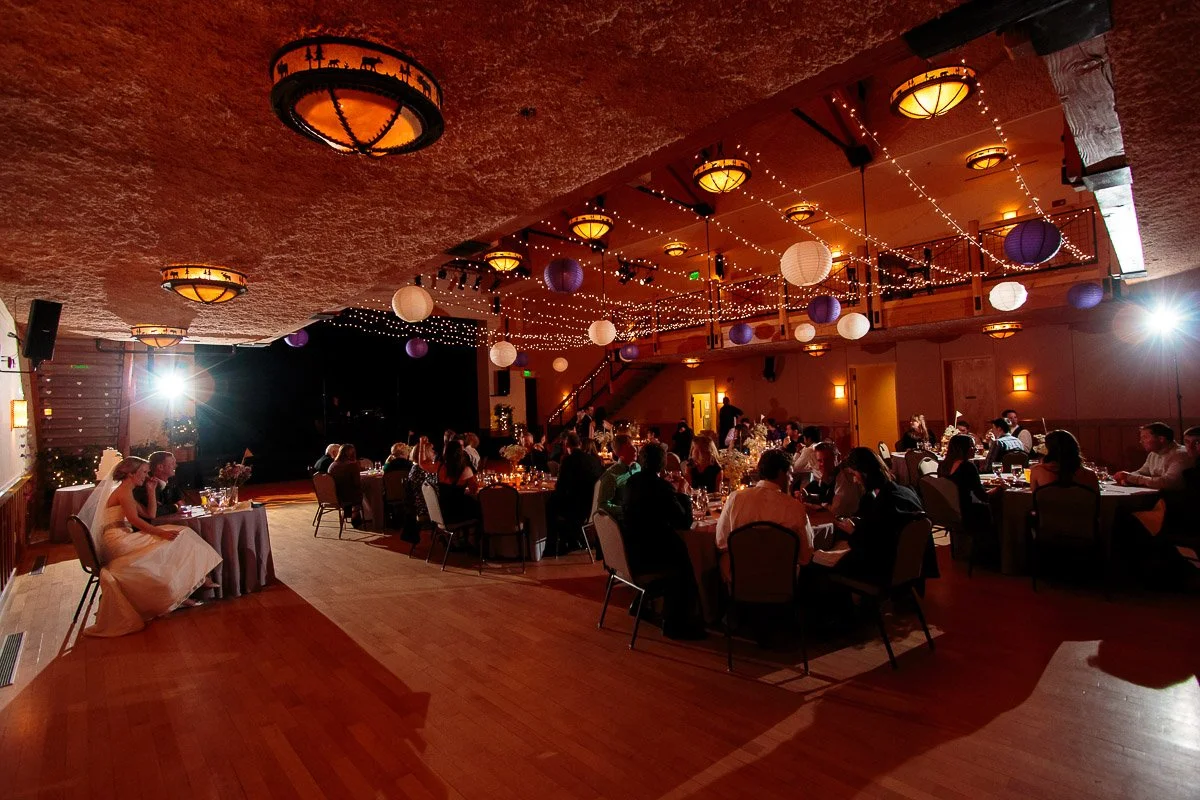 A warmly lit Silverthorne Pavilion wedding reception with round tables and seated guests. String lights and lanterns hang above, creating an inviting, festive atmosphere 