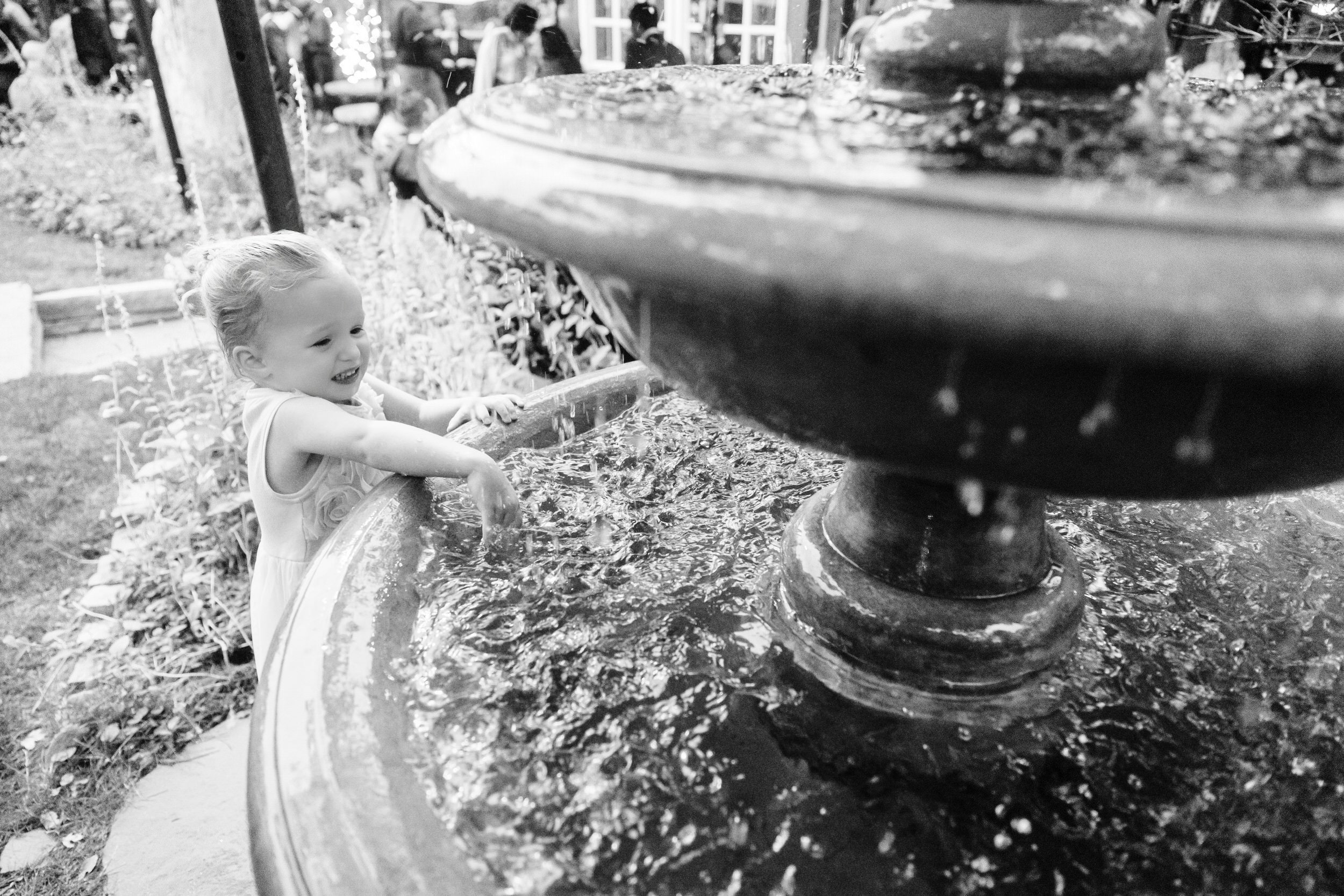 A young girl splashes water and plays in the fountain during the cocktail hour at a Greenbriar Inn wedding in Boulder, Colorado
