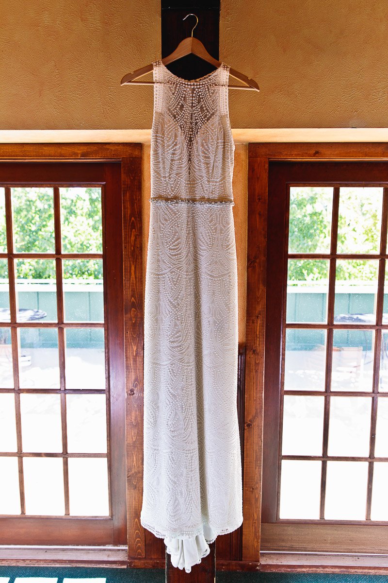 Elegant white wedding dress with intricate beadwork hangs on a wooden door, framed by sunlight streaming through glass panes, creating a serene and romantic ambiance.