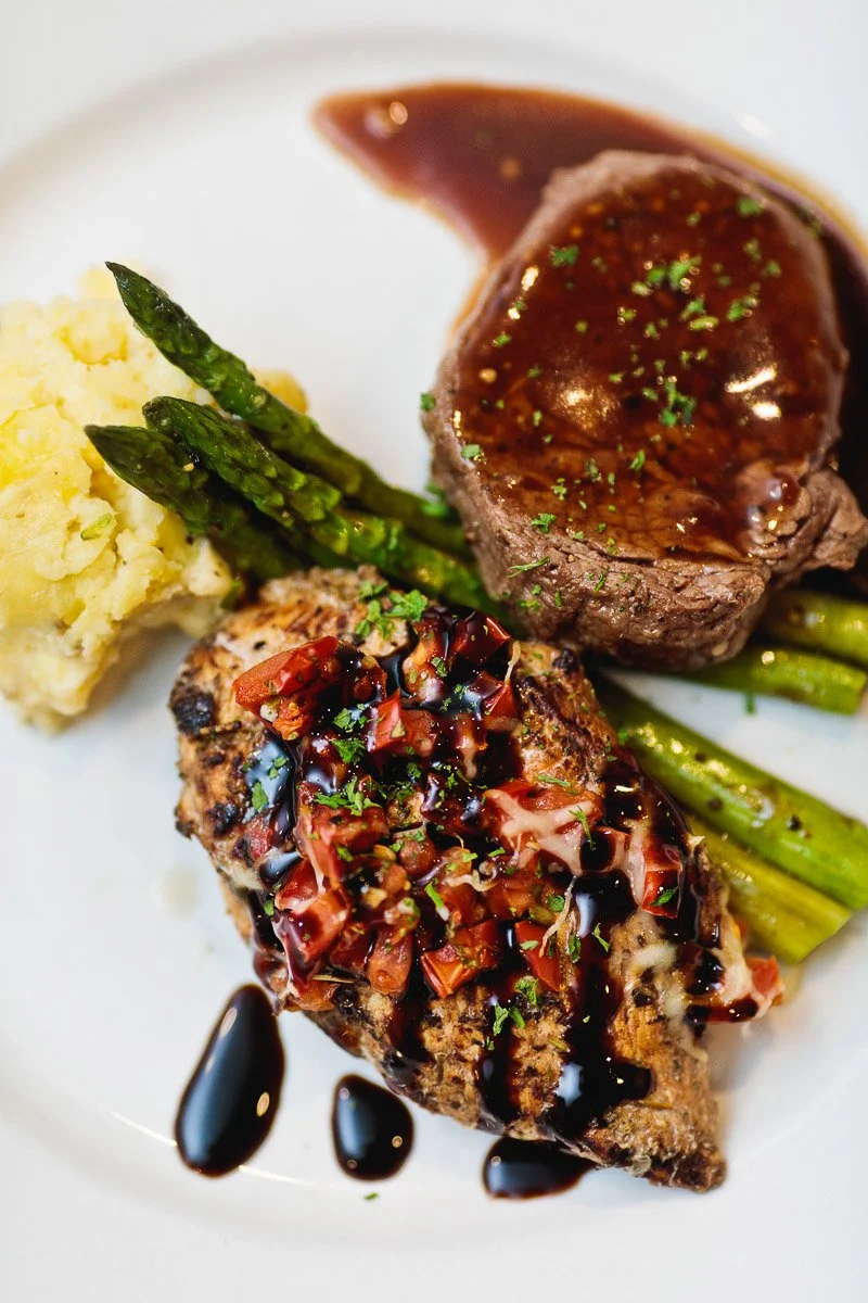 A gourmet plate features juicy steak with rich brown sauce, grilled chicken drizzled with balsamic glaze, mashed potatoes, and vibrant asparagus.