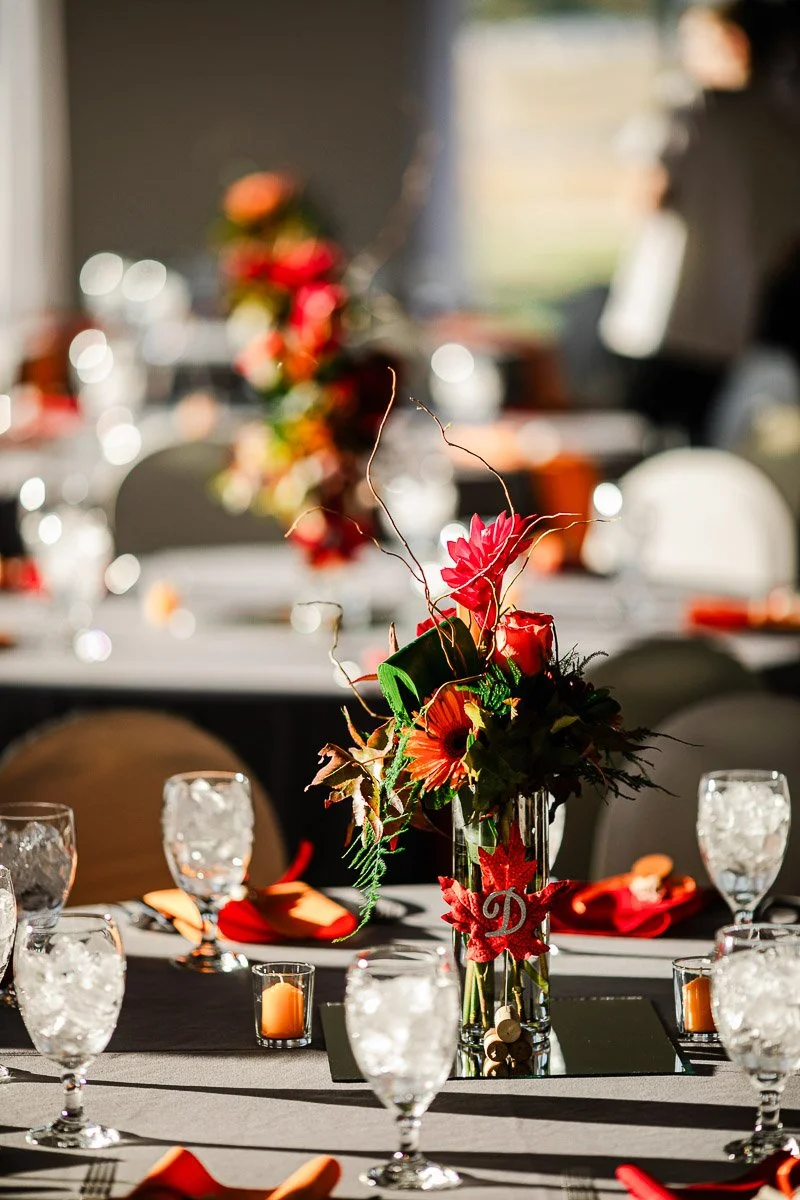 Blurred banquet hall with elegantly set tables, featuring vibrant floral centerpieces, red napkins, and glistening glassware, creating a festive atmosphere.