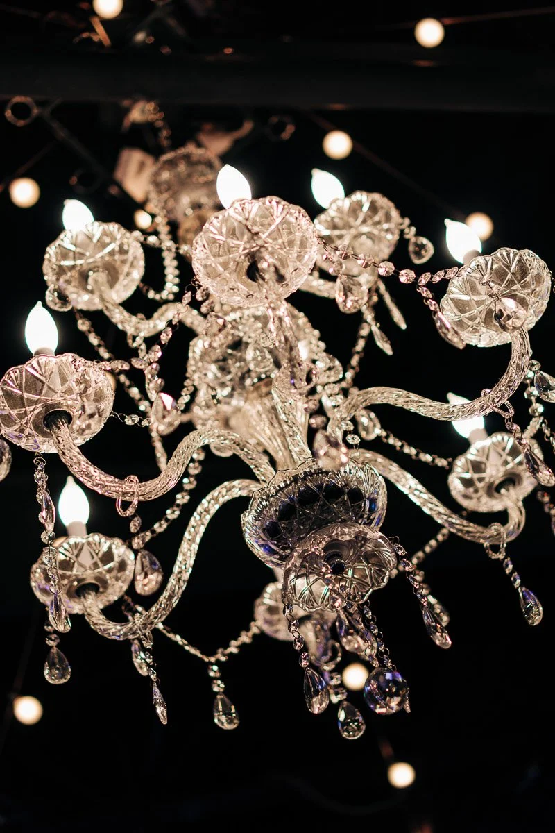 A sparkling crystal chandelier with intricate details, lit candles, and hanging crystals against a black background, creating a luxurious and elegant atmosphere.