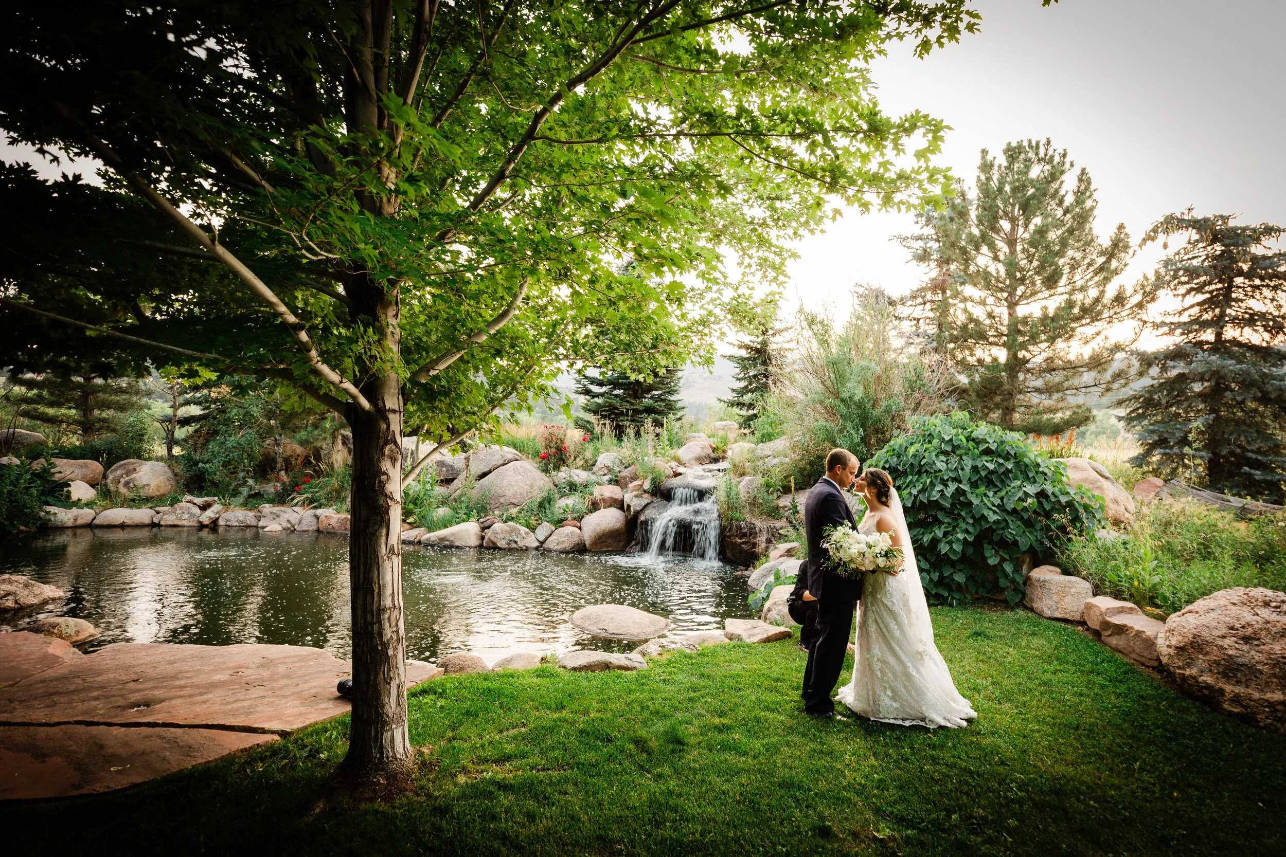 Bride and groom kiss next to the fountain and pond in soft Summer evening light during a Greenbriar Inn wedding reception in Boulder, Colorado