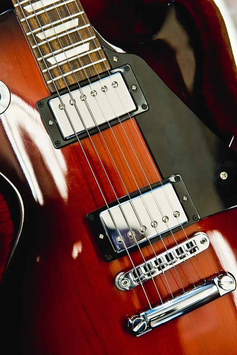Close-up of a red electric guitar with chrome pickups and bridge, highlighting its glossy finish and sleek contours, evoking a classic rock vibe.