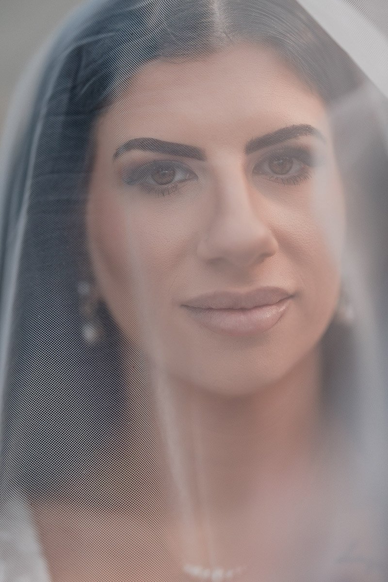 Close-up of a bride looking serene, her face softly veiled. The makeup is elegant, with focus on her eyes and lips, conveying a calm and joyful mood.
