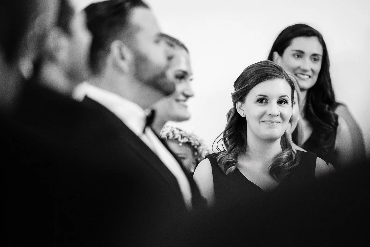 A black-and-white photo features a group of smiling people at an event. A woman in the foreground appears pleased and engaged, creating a joyful atmosphere.