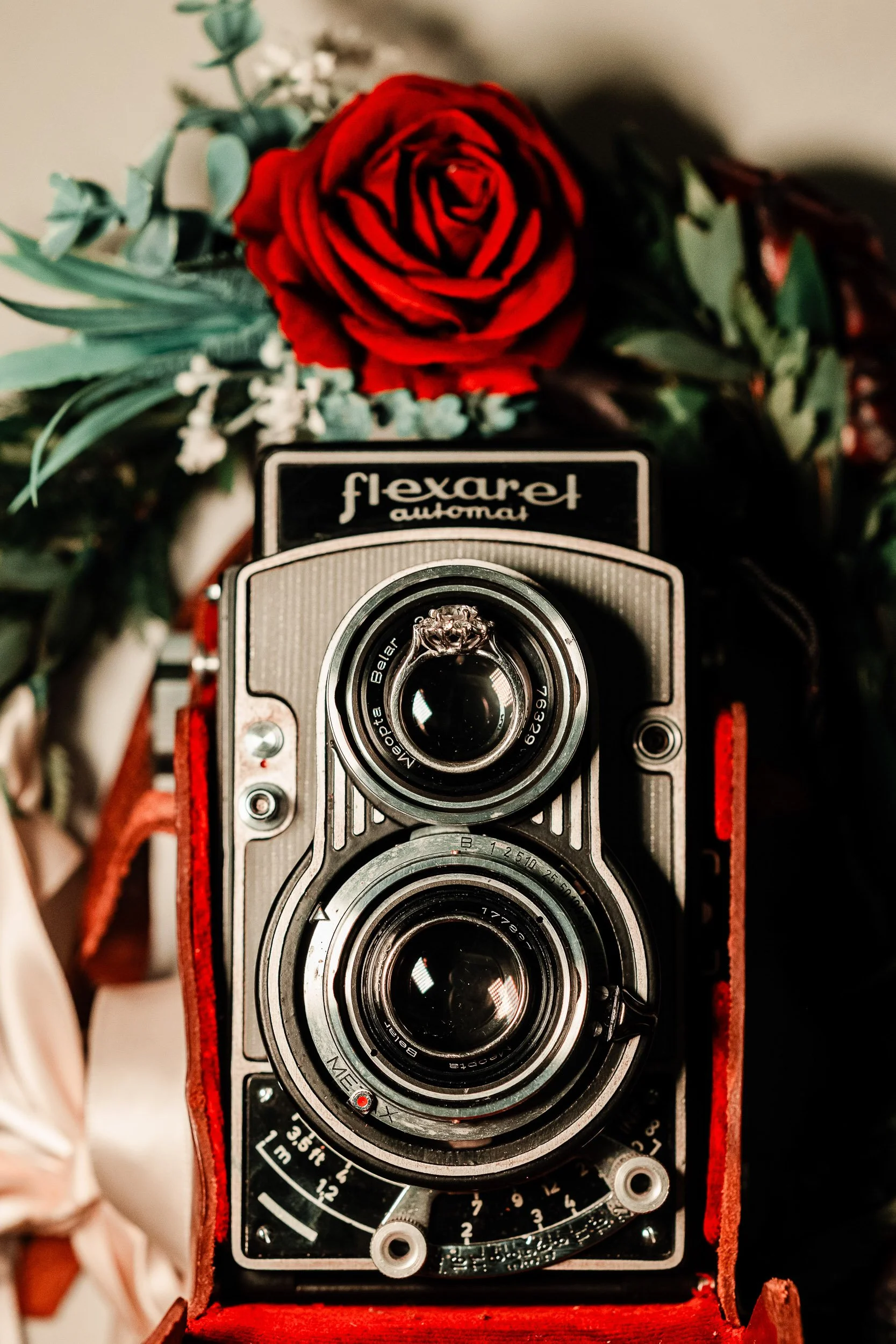 Two wedding rings set respectively on a twin-lens reflex film camera with a rose during a Black Canyon Inn wedding reception in Boulder, Colorado