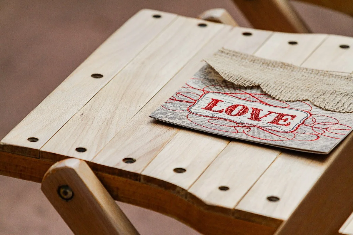 A wooden chair holds a card with a burlap flap and the word "LOVE" in red. The setting feels warm and rustic, emphasizing a theme of affection.
