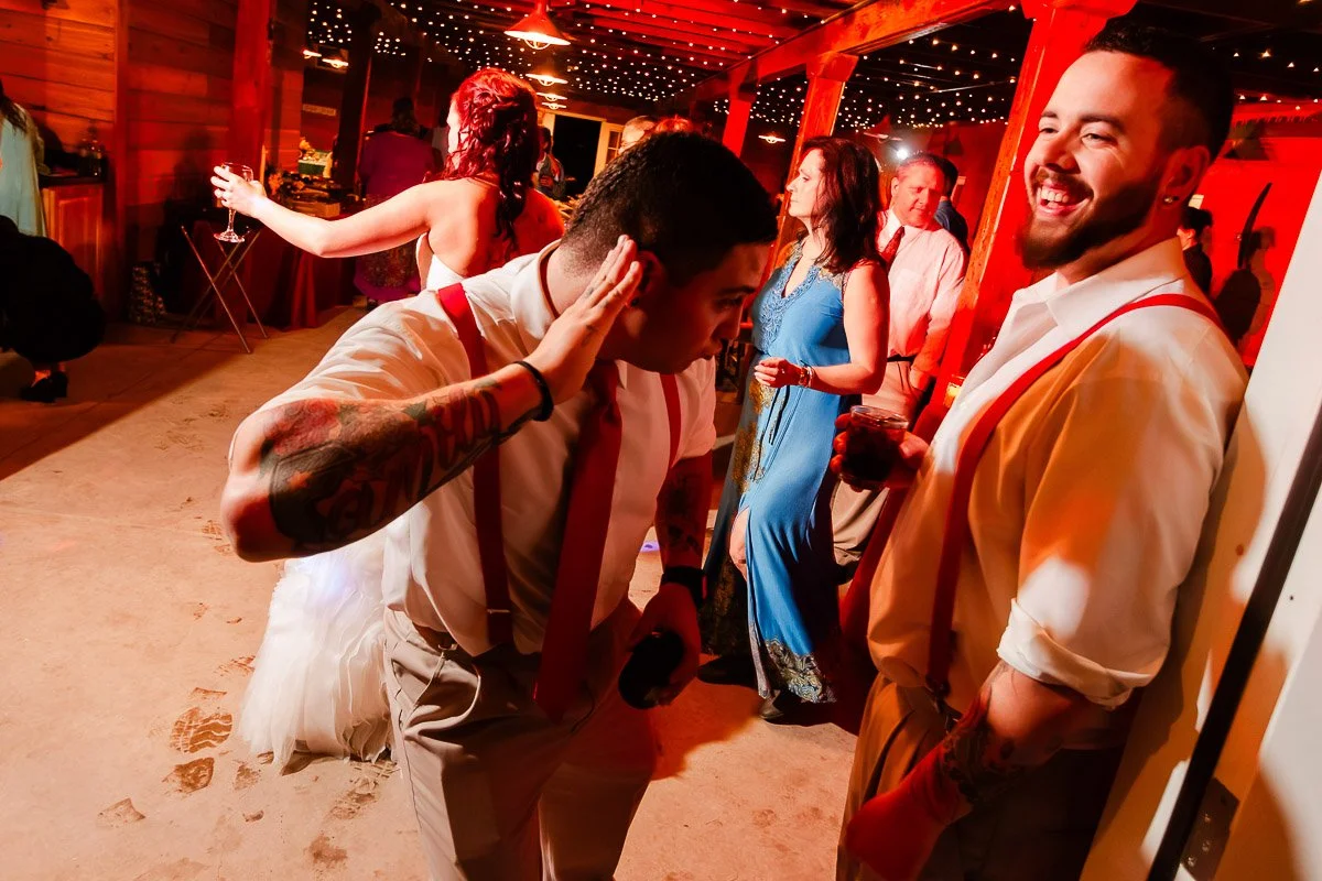 Individuals in formal wear celebrate at a lively dance party, warmly illuminated with red tones, featuring laughter, joy, and festive string lights.
