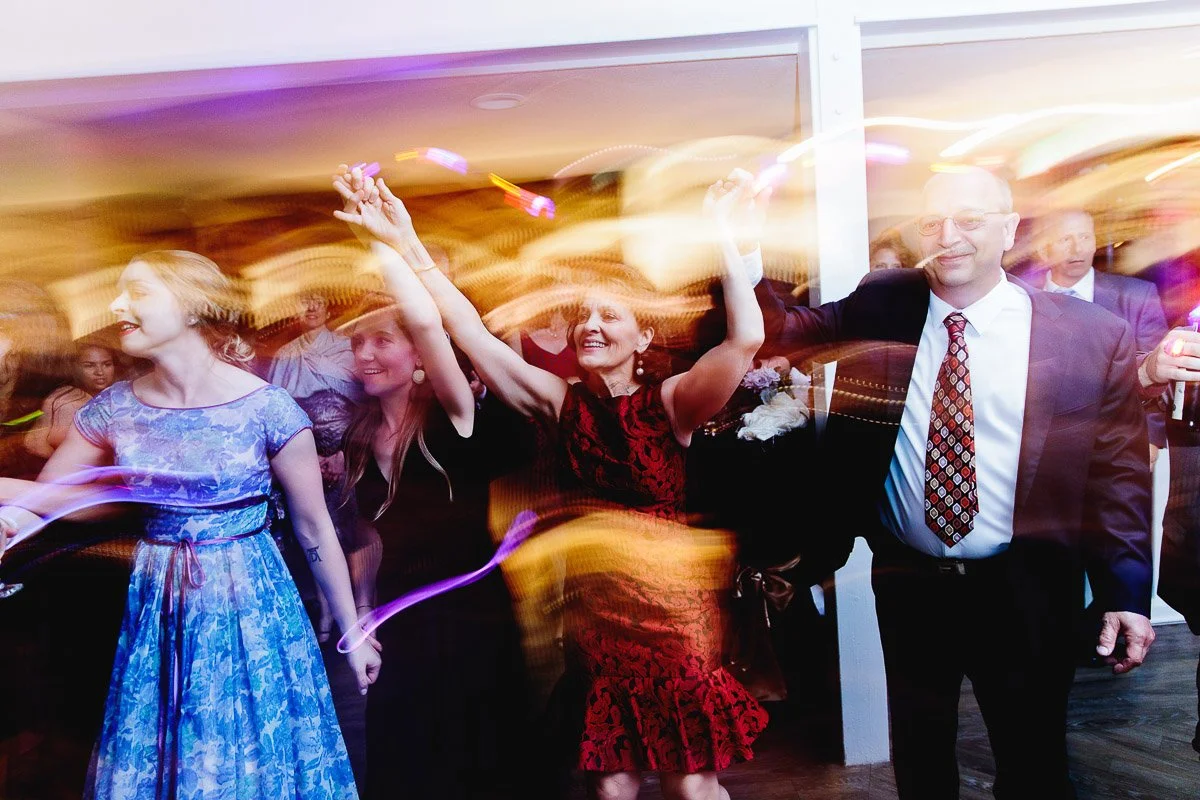 People in festive attire dance energetically in a blurred motion, creating a dynamic, joyful atmosphere with colorful light trails in the background.