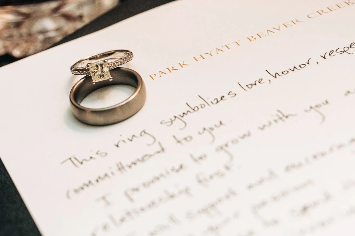 Close-up of wedding rings on a letter with elegant handwriting. One ring has a large diamond, and the note conveys themes of love and commitment.