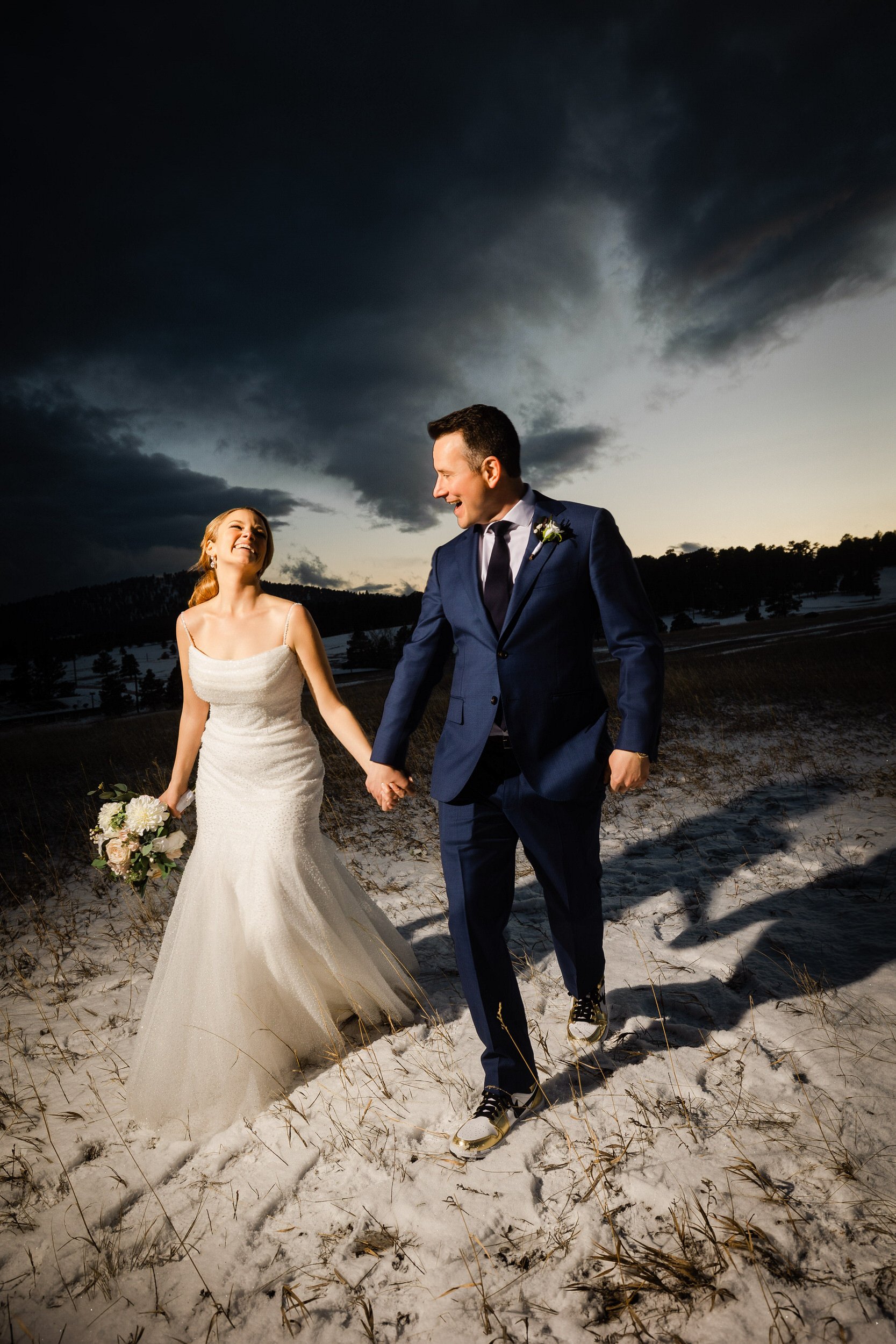 Bride and groom walk holding hands through a snowy field during a Winter Mount Vernon Canyon Club wedding in Golden, Colorado