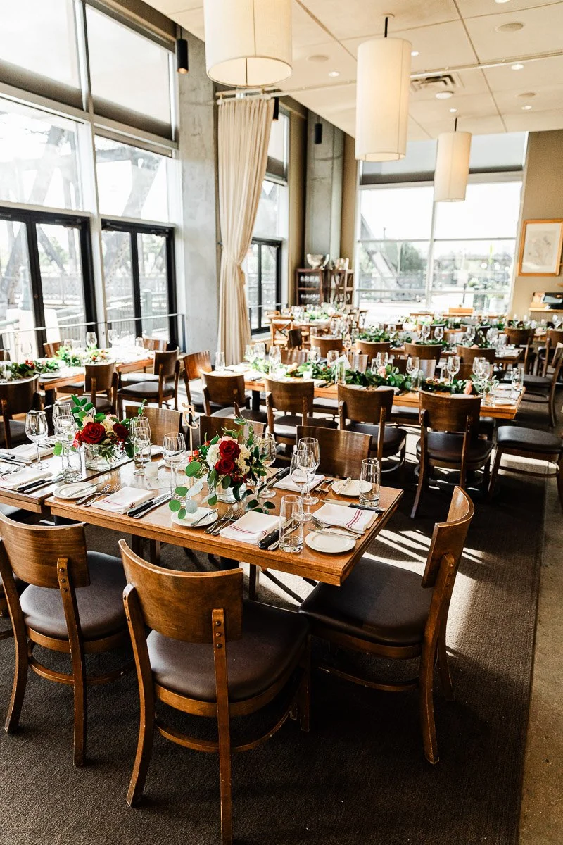 Elegant Coohills restaurant interior with wooden tables set for dining, featuring red and white floral centerpieces and large windows letting in natural light.