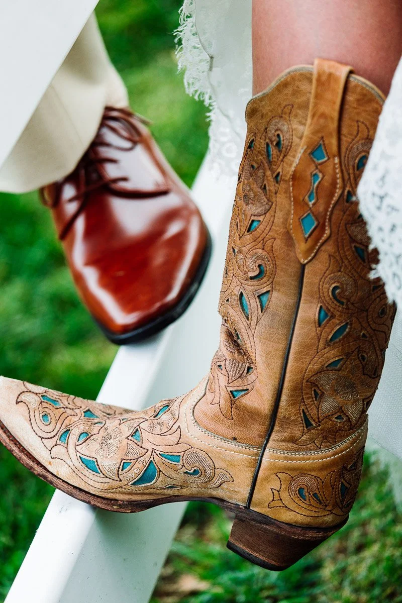 Close-up of a pair of shoes on a grassy background: one brown polished dress shoe and one tan cowboy boot with turquoise inlays and intricate patterns.