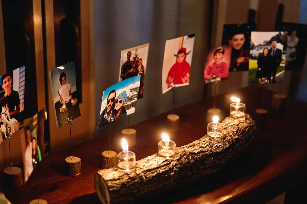 A series of family photos are displayed on stands behind a log with tea light candles. The warm glow creates a nostalgic and intimate atmosphere.