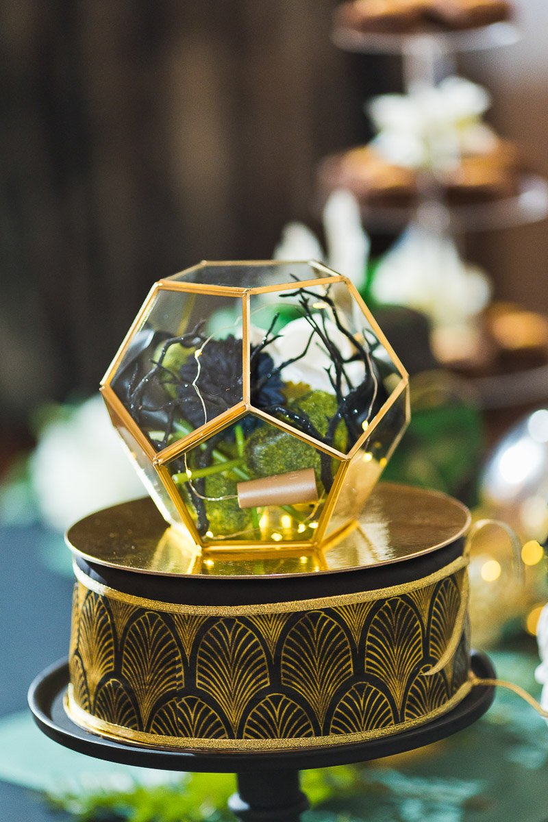 A geometric terrarium with plants sits on a decorative gold and black stand. The scene is blurred in the background, creating an elegant, modern ambiance.