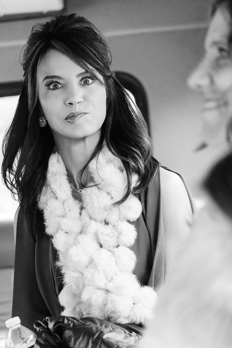 Black and white image of a woman with long dark hair wearing a fluffy scarf, playfully making a pouty face in conversation, exuding a lighthearted mood.