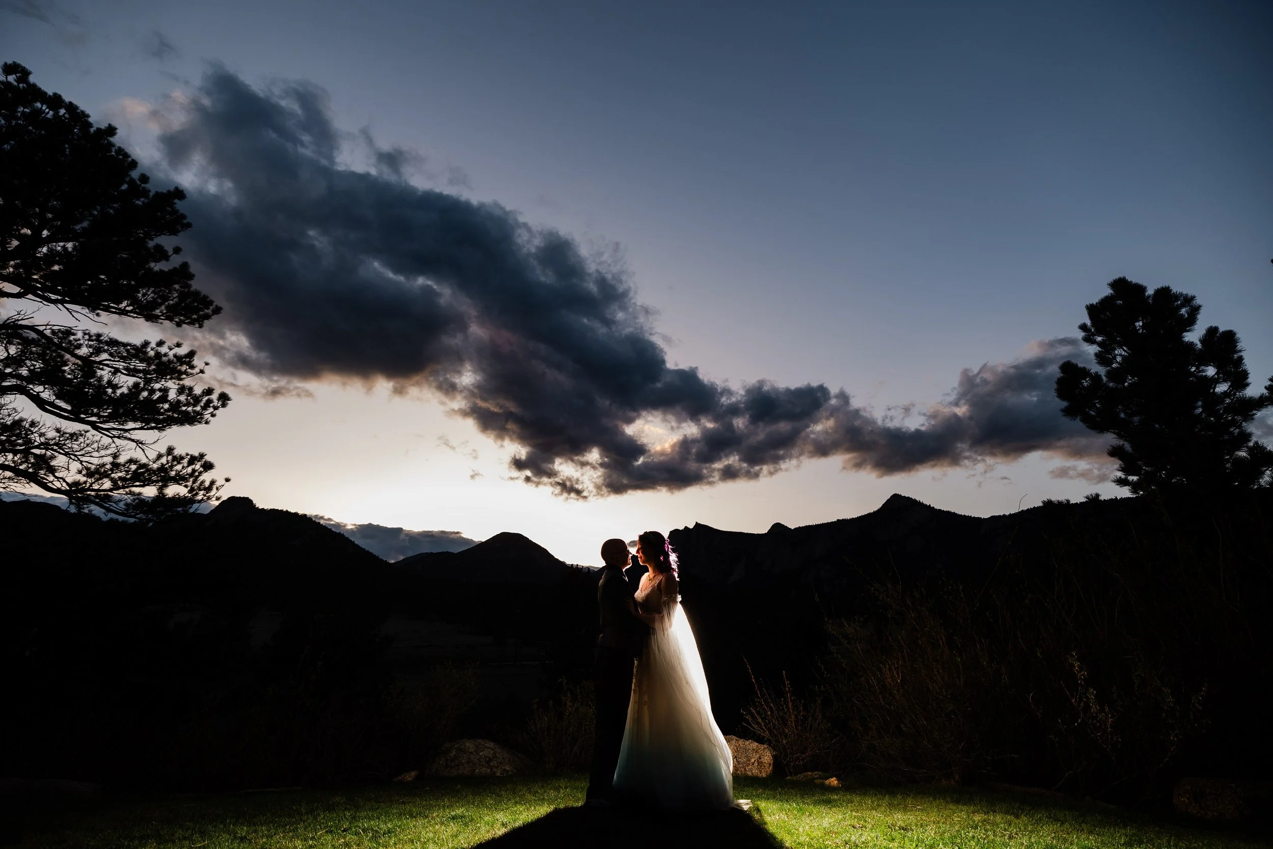 A bride and groom embrace in front of a post sunset alpine glow during a Black Canyon Inn wedding reception in Estes Park, Colorado