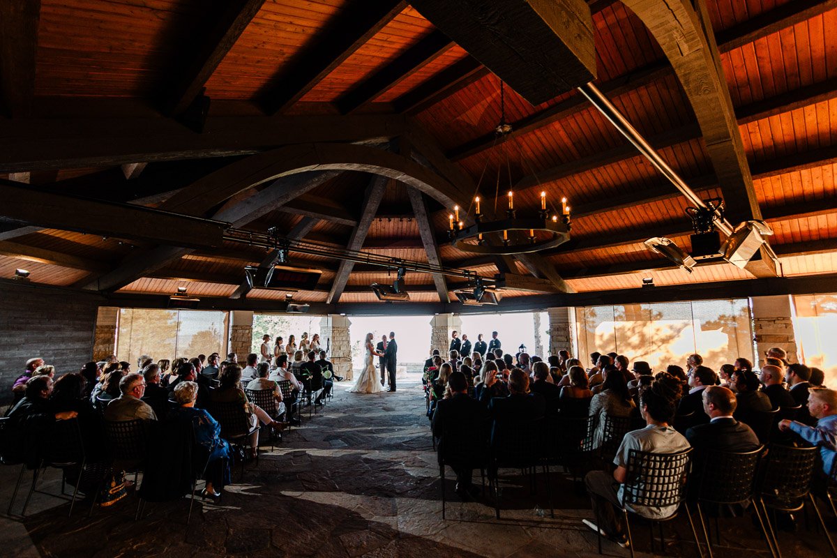 Wedding ceremony in a rustic wooden pavilion with vaulted ceiling. Guests seated facing the couple at the altar, creating an intimate, warm atmosphere during a Sanctuary Golf Course wedding in Sedalia, Colorado.