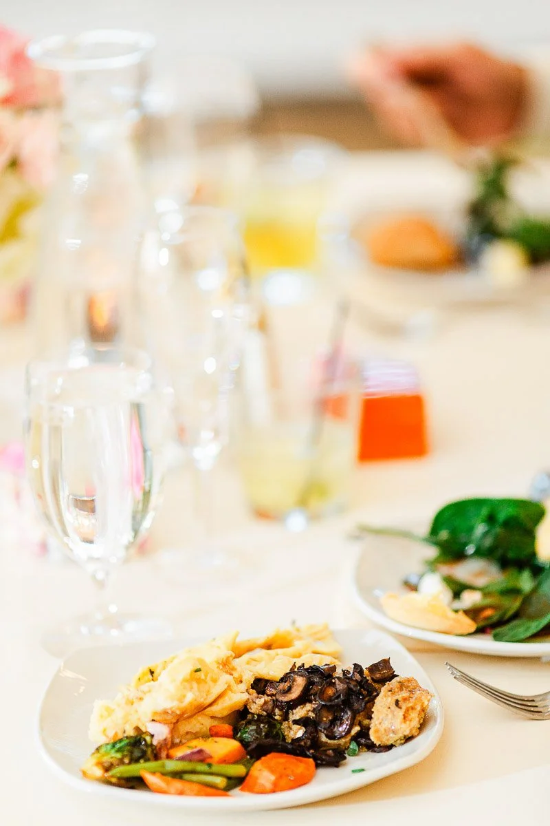 A table setting with a plate featuring scrambled eggs, sautéed mushrooms, and colorful vegetables. A glass of water and blurred dining elements are in the background.
