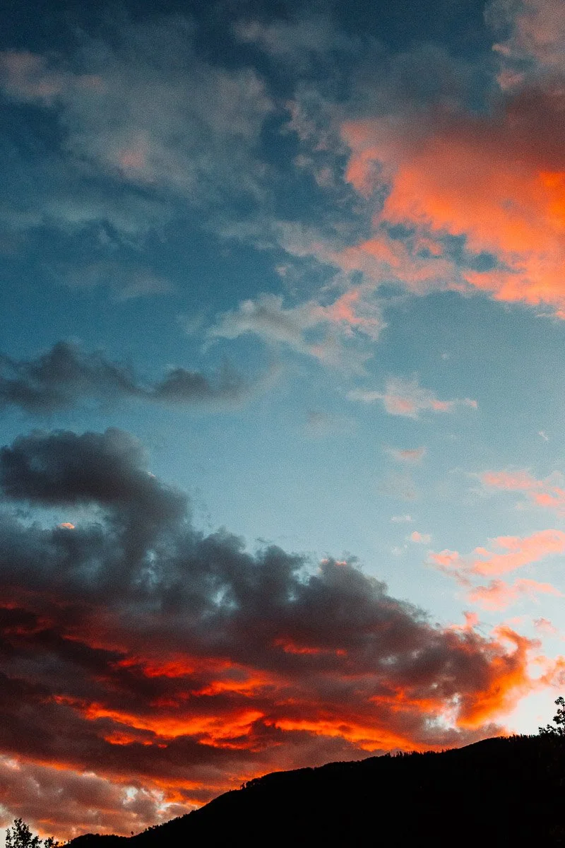 Dramatic sunset with vibrant orange and red clouds against a blue sky, silhouetting a dark mountain range, evoking a sense of calm and wonder.