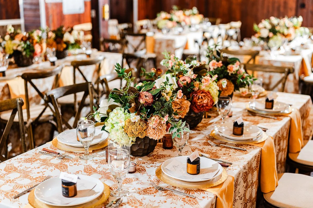 Elegant banquet setup with floral centerpieces on patterned tablecloths. Plates and glasses neatly arranged, conveying a warm, festive ambiance.